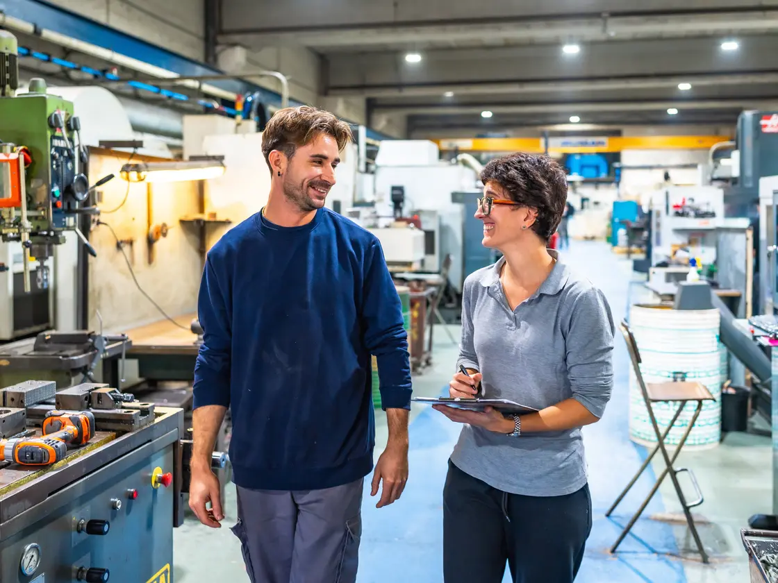 A manager walking a new team member through the workshop floor, tablet in hand