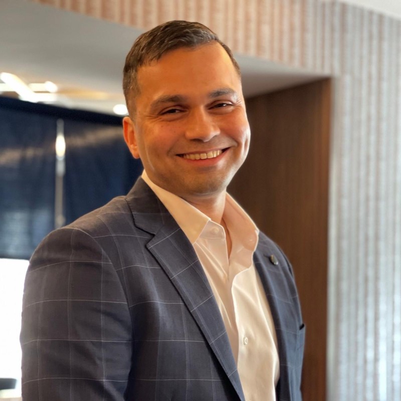 Muks Syed, founder of HookedGrowth, smiling in a navy check blazer